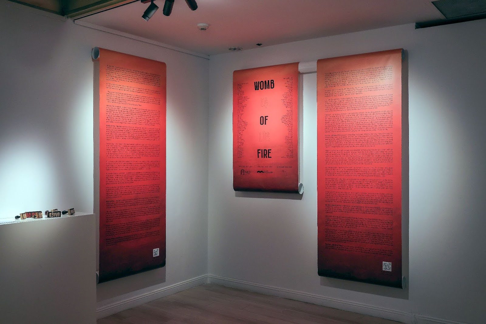 View of an exhibition install with sheets of red paper hung on white walls with text