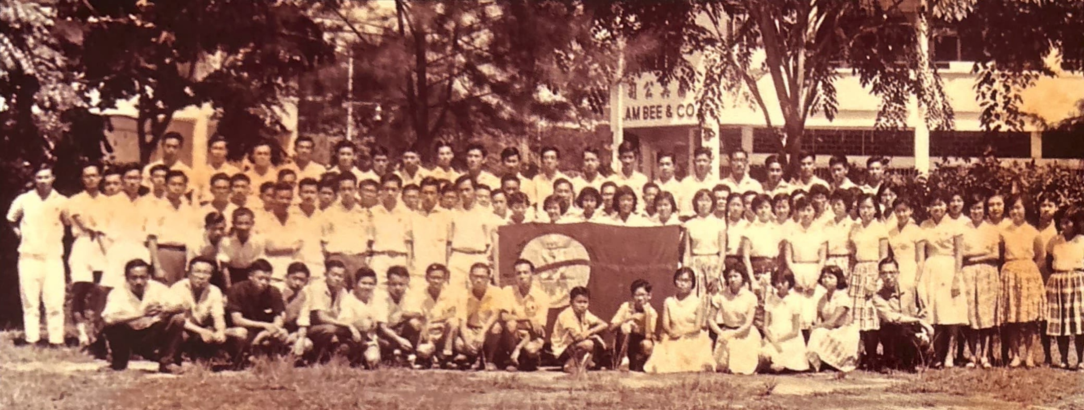 A faded group photo of people sitting and standing in front of trees.